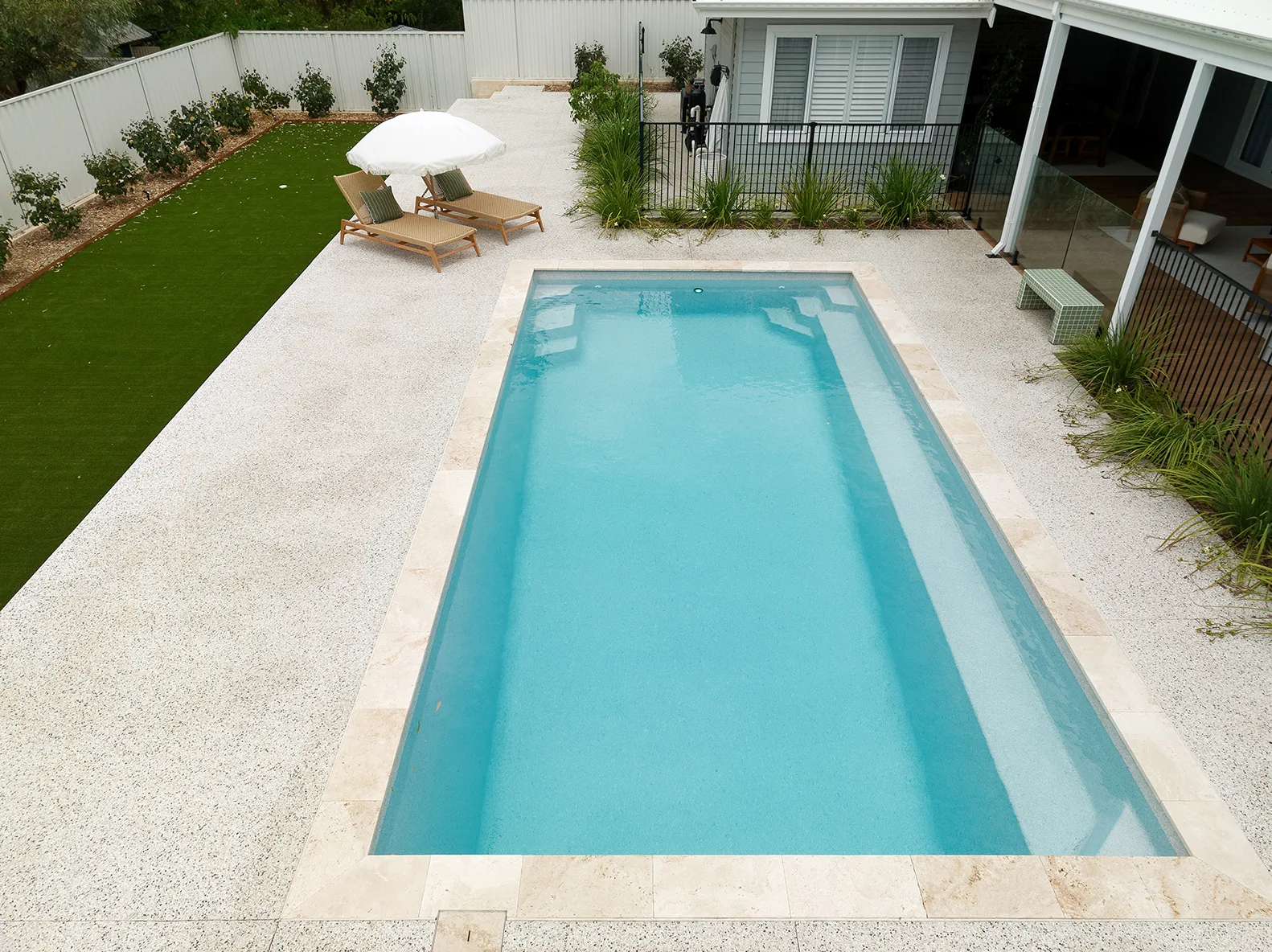 Completed Entertainer 8m fibreglass pool with travertine coping, poolside loungers and a garden lawn