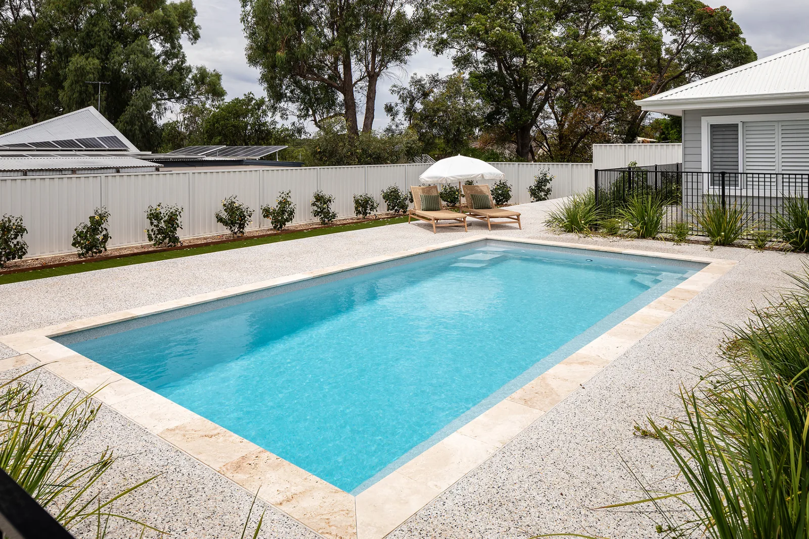 Completed Entertainer 8m fibreglass pool viewed along its length with paved surrounds and poolside loungers