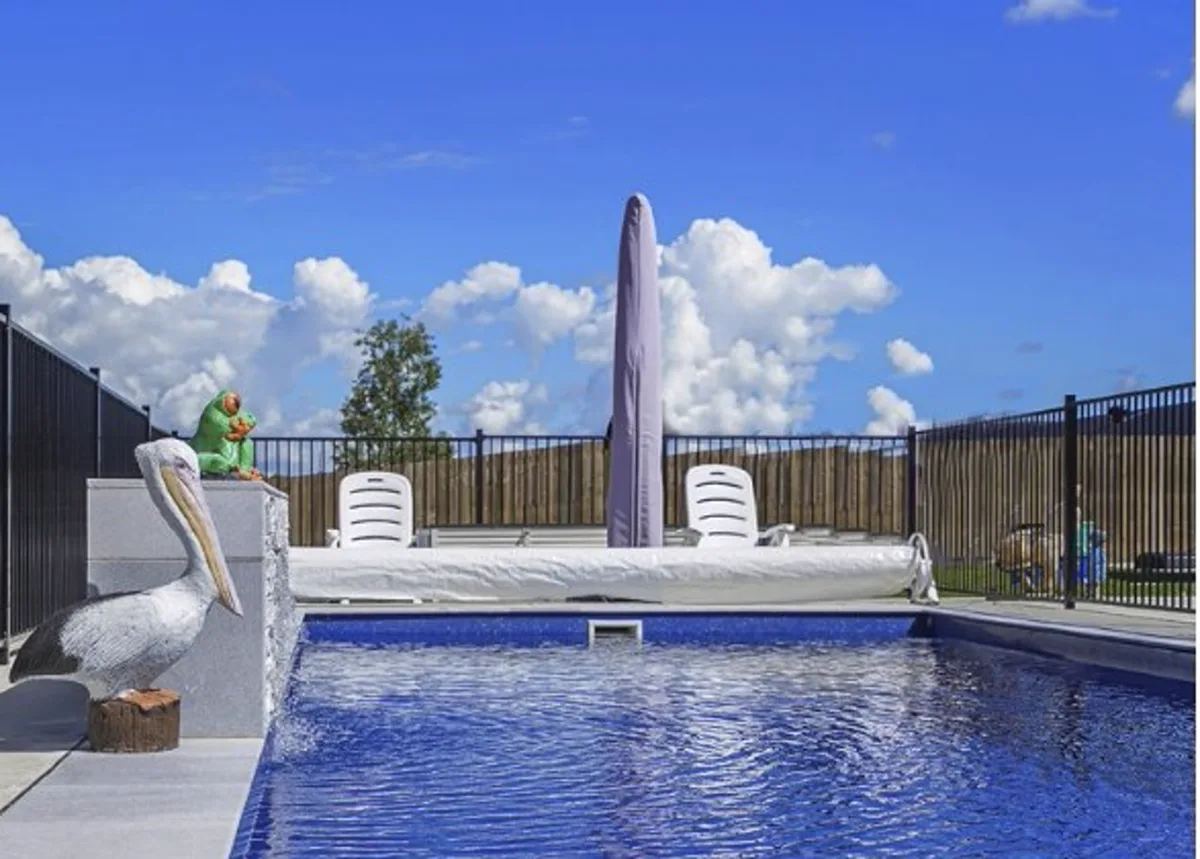 Platinum 10m fibreglass pool with a sheet waterfall, light-grey paved surrounds and black pool fencing