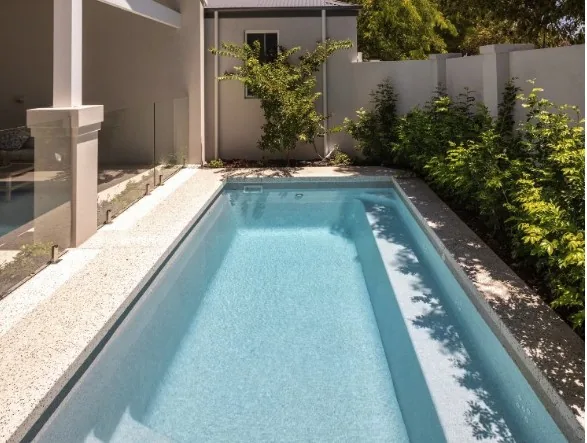 Dolphin 11m fibreglass pool with a full-length bench seat beside glass fencing and garden beds
