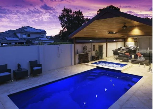 Platinum 7m fibreglass pool lit up at dusk beside an entertaining pavilion