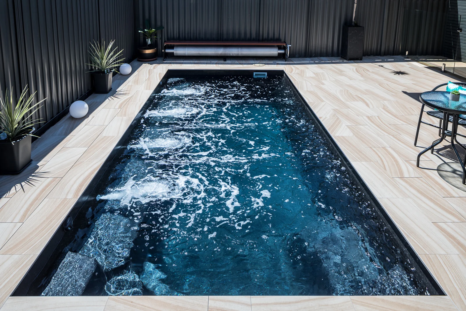 Completed Entertainer 7m fibreglass pool viewed lengthwise with bubbling water and tiled surrounds
