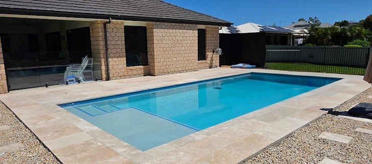 Fibreglass pool with travertine paving and glass fencing
