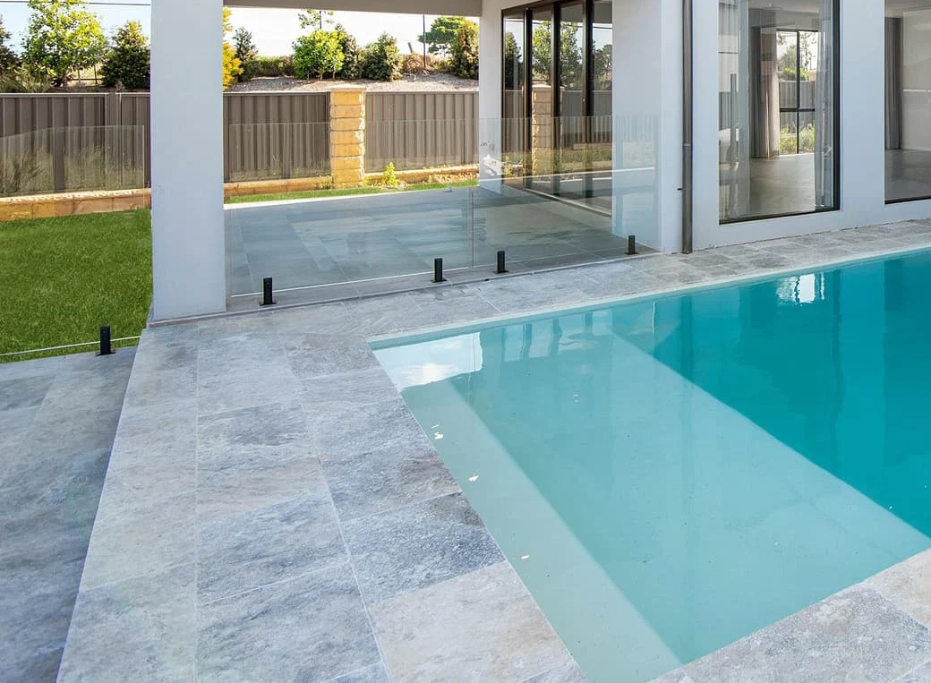 Modern pool with stone paving and glass fencing beside contemporary home